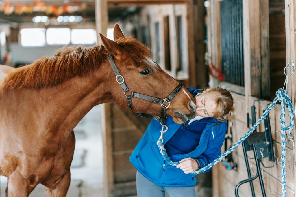 Woman affectionately interacting with horse in a stable, showcasing human-animal bond.